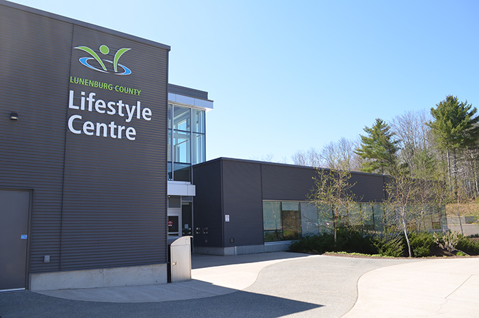 Outside of the Lunenburg County Lifestyle Centre; a big, brown building with several trees in front of it.