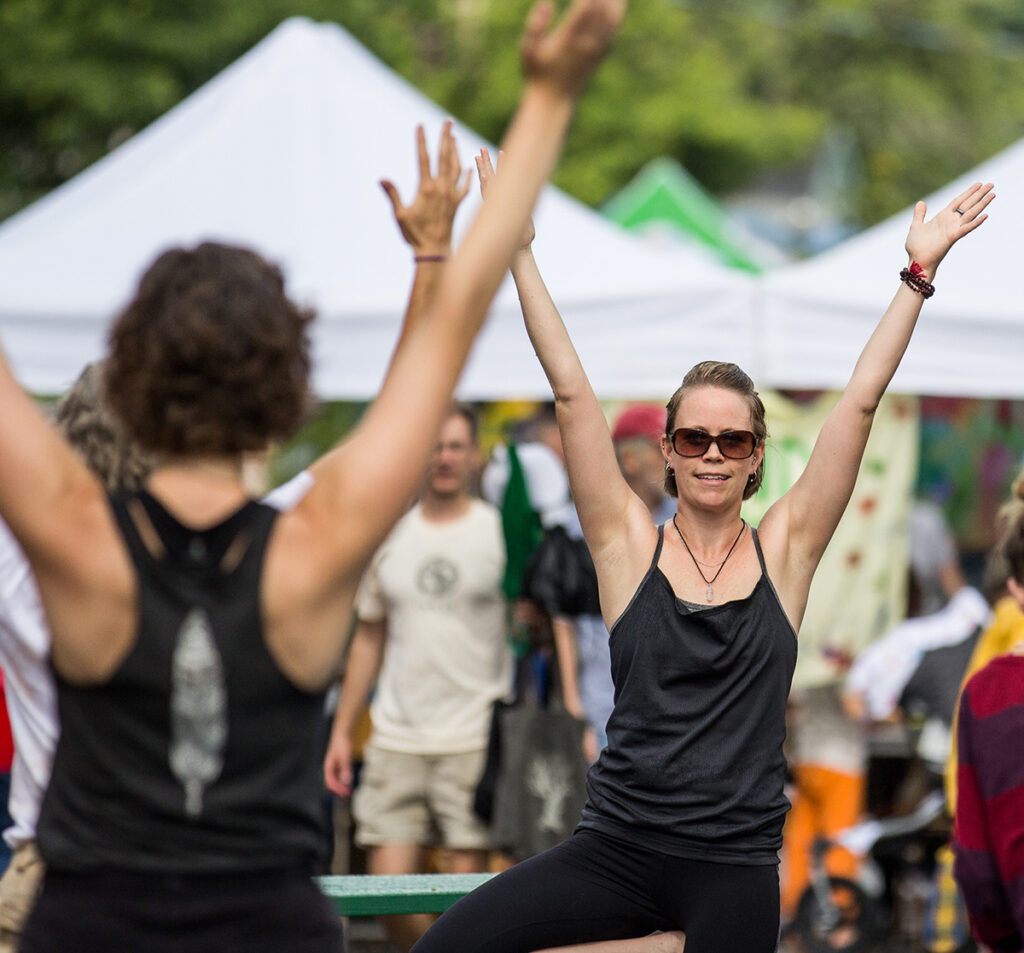Two women holding yoga poses and a crowded street during a festival.