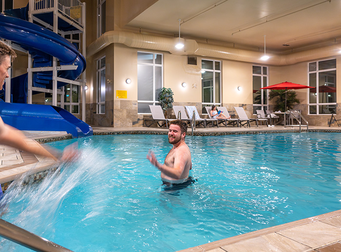 Indoor hotel pool with waterslide and guests swimming and relaxing poolside.
