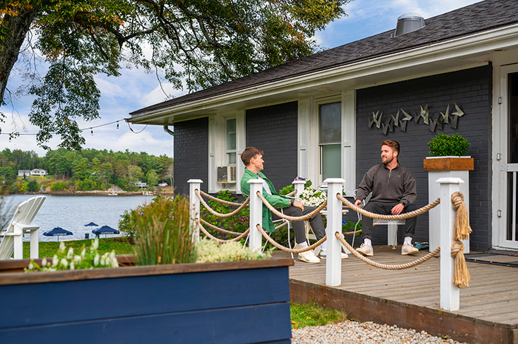 Two people relaxing on a patio overlooking the water beside a riverfront cottage.