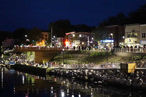 A nighttime view of a festival on the LaHave River. Crowds of people are seen on the dimly lit streets.