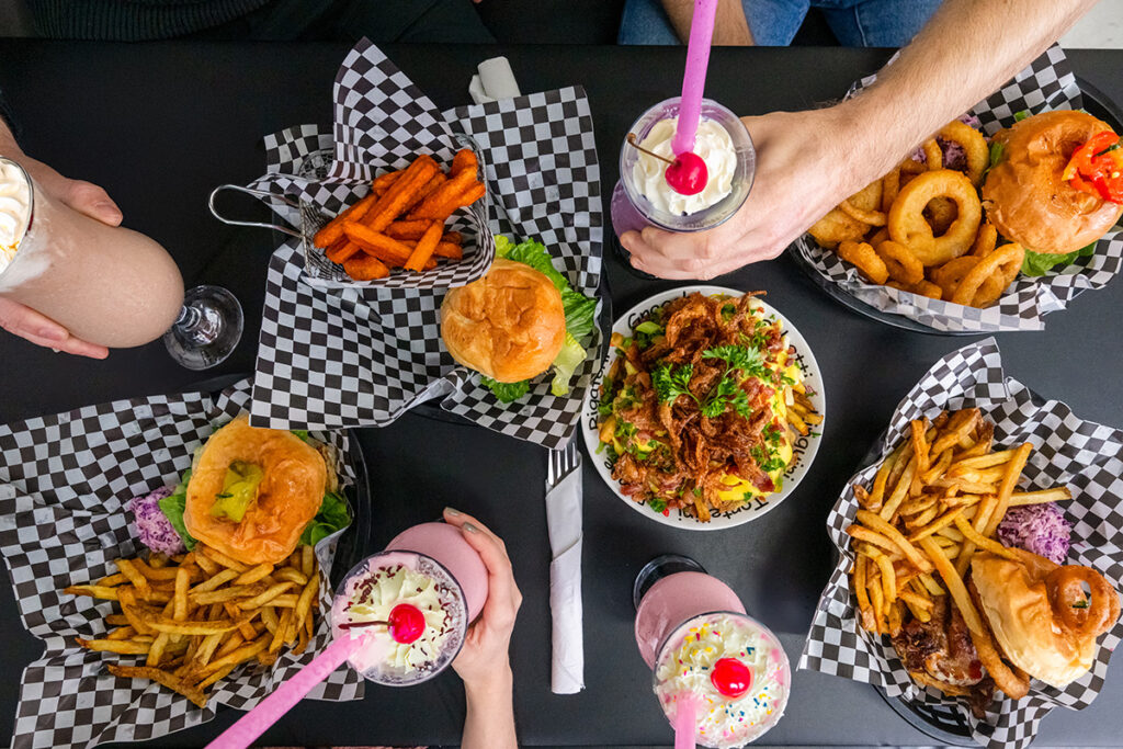 Burgers, fries, onion rings, milkshakes, and loaded fries served on a restaurant table.