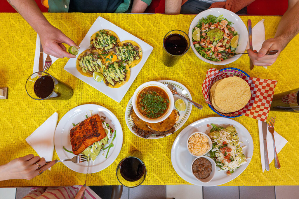 Several Mexican dishes are laid out on a bright yellow table.