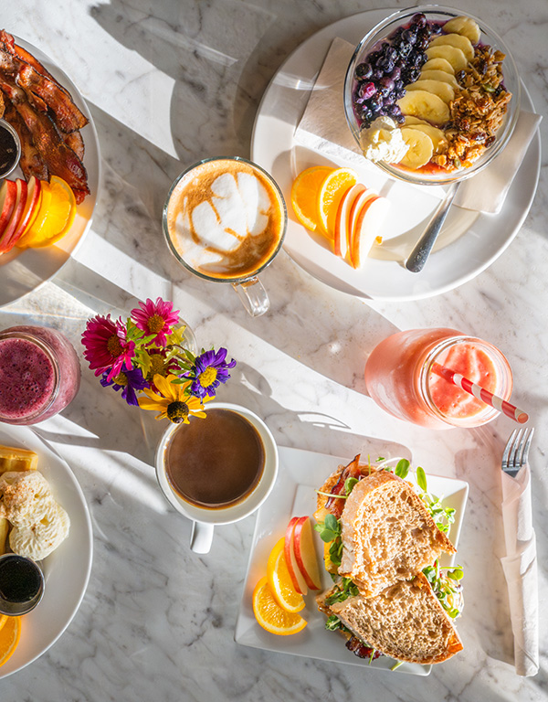 A top-down image of a brightly-lit table with several beverages and plates of breakfast food.