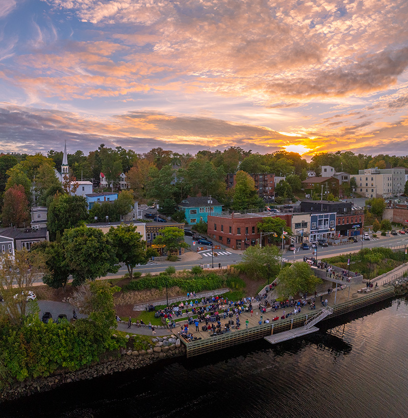 Aerial view of Bridgewater’s LaHave River waterfront at sunset with crowds gathered at Shipyards Landing.