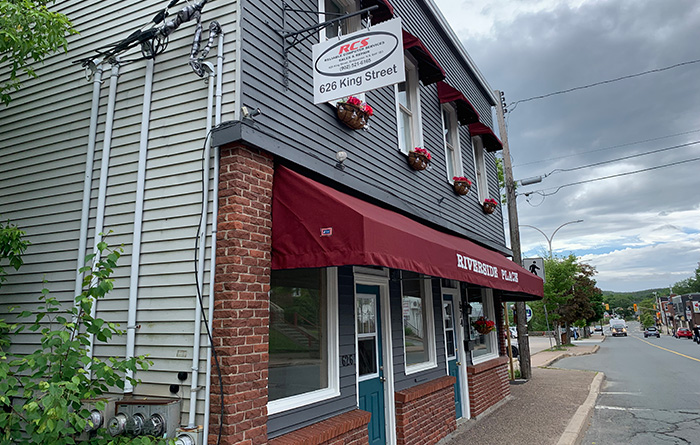 Building along King Street in Bridgewater. A red awning hangs over a brick-covered front entrance that reads, "Riverside Place".